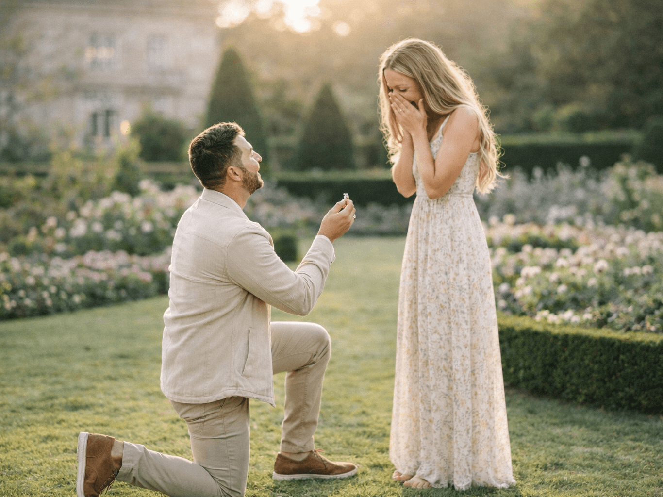 man down on one knee proposing to a woman in a stately home garden